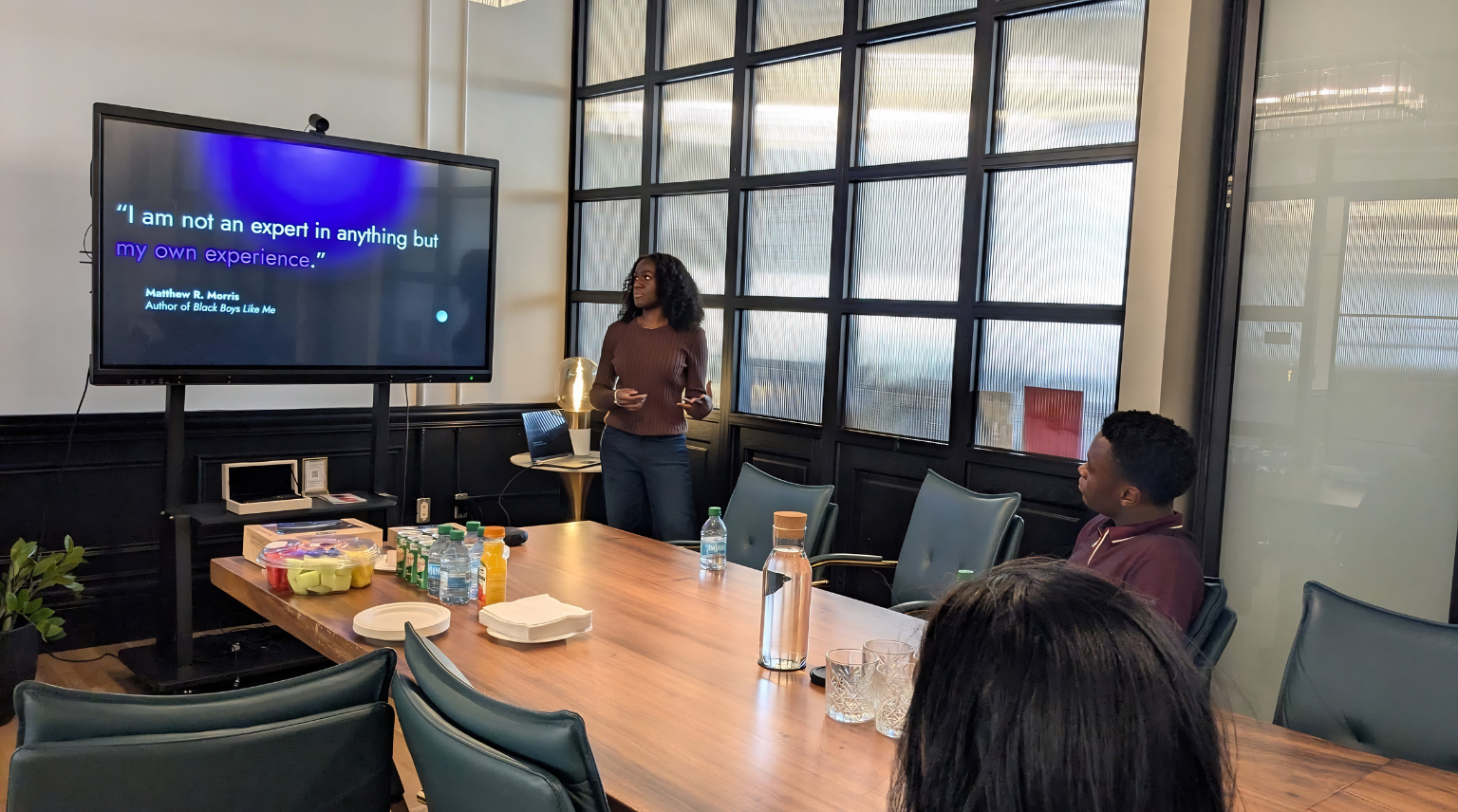 Person presenting in a conference room with a large screen displaying text.